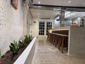 A bar area with stools and a counter, a door with frosted glass panels, and a wall with a textured pattern. - The Self-Sustainable Beach House (South Padre Island)