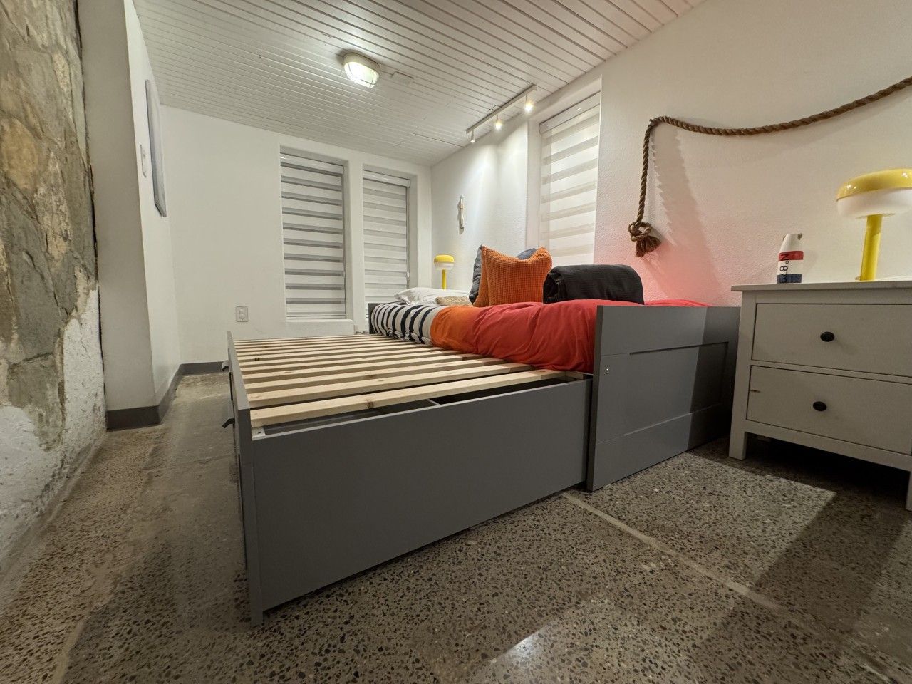 Ein Schlafzimmer mit einem Bett, einem Schminktisch, einer Lampe und einem Fenster mit Jalousien.