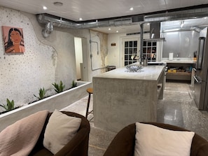A modern kitchen with a central island, stainless steel appliances, and a dining area with two sofas. - The Self-Sustainable Beach House (South Padre Island)