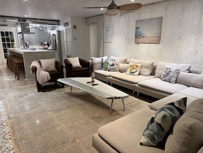 A modern living room with a sofa, armchairs, a coffee table, and a kitchen area in the background. - The Self-Sustainable Beach House (South Padre Island)