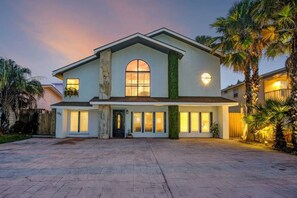 A two-story house with a large front porch, a stone column, and a circular window. - The Self-Sustainable Beach House (South Padre Island)