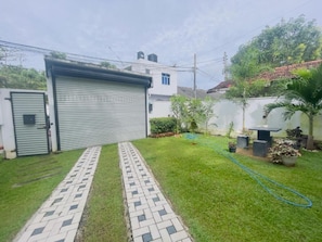 Un patio trasero residencial con un camino pavimentado, un garaje y una pequeña zona ajardinada con plantas en macetas.