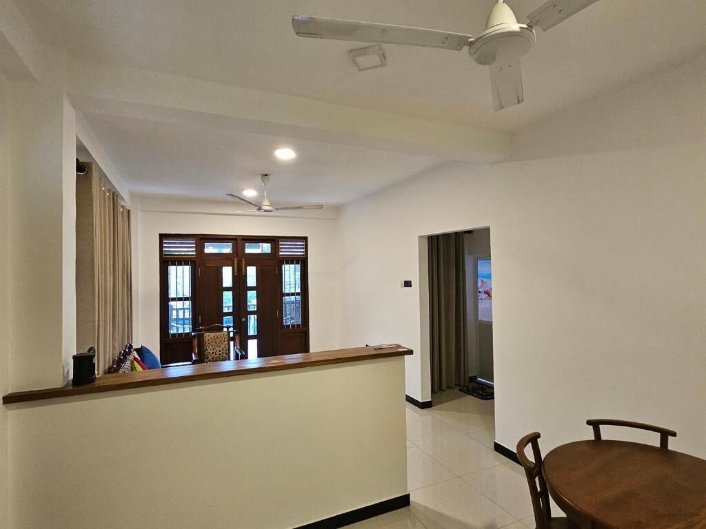 Eine Hotelhalle mit einer Rezeption, einem Essbereich mit Stühlen und einem Deckenventilator.