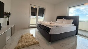 A modern bedroom with a bed, a flat-screen TV, a small table, and a door leading to a balcony. - Vila Gaia (Federacija Bosne i Hercegovine)