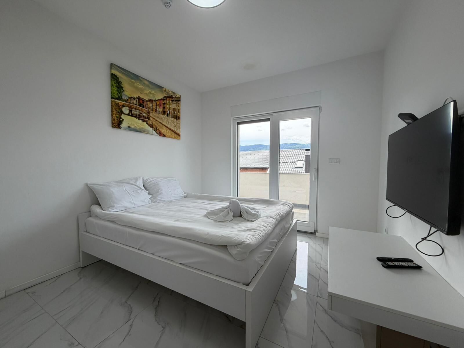 Une chambre à coucher moderne avec un lit, un téléviseur et un tableau accroché au mur.