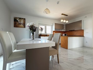 Una cocina moderna con zona de comedor, que incluye una mesa blanca, sillas y un jarrón con flores.