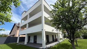 A modern multi-story building with a flat roof, a covered outdoor area, and a well-maintained lawn.