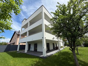 Un edificio moderno de varios pisos con techo plano, un área exterior cubierta y un césped bien cuidado.