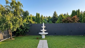 A garden with a white fountain, a stone pathway, and a dark fence.