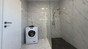 A compact bathroom with a washing machine, a glass shower enclosure, and a tiled floor. - Vila Gaia (Federacija Bosne i Hercegovine)