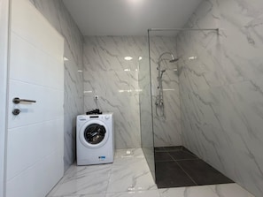 Un baño pequeño con lavadora, cabina de ducha de vidrio y piso de baldosas.
