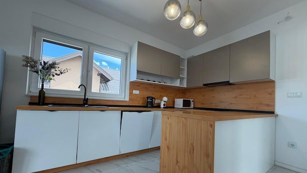 A modern kitchen with a central island, white cabinetry, and a wooden countertop.