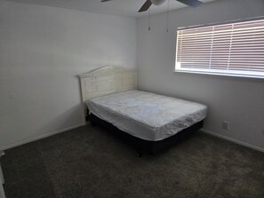 A small, single-bed room with a white headboard, a ceiling fan, and a window with blinds.