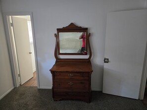 Una cassettiera in legno con uno specchio in una stanza con pavimento rivestito di moquette e pareti bianche.