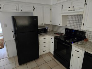 A kitchen with white cabinets, a black refrigerator, a microwave, a stove, and a tiled backsplash.