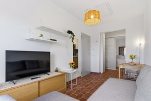 Ein modernes Wohnzimmer mit einem Flachbildfernseher, einer Couch, einem kleinen Tisch und einer Pendelleuchte.