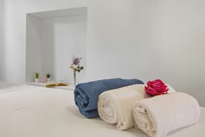 Ein ordentlich bezogenes Bett mit aufgerollten Handtüchern und einer Rose.