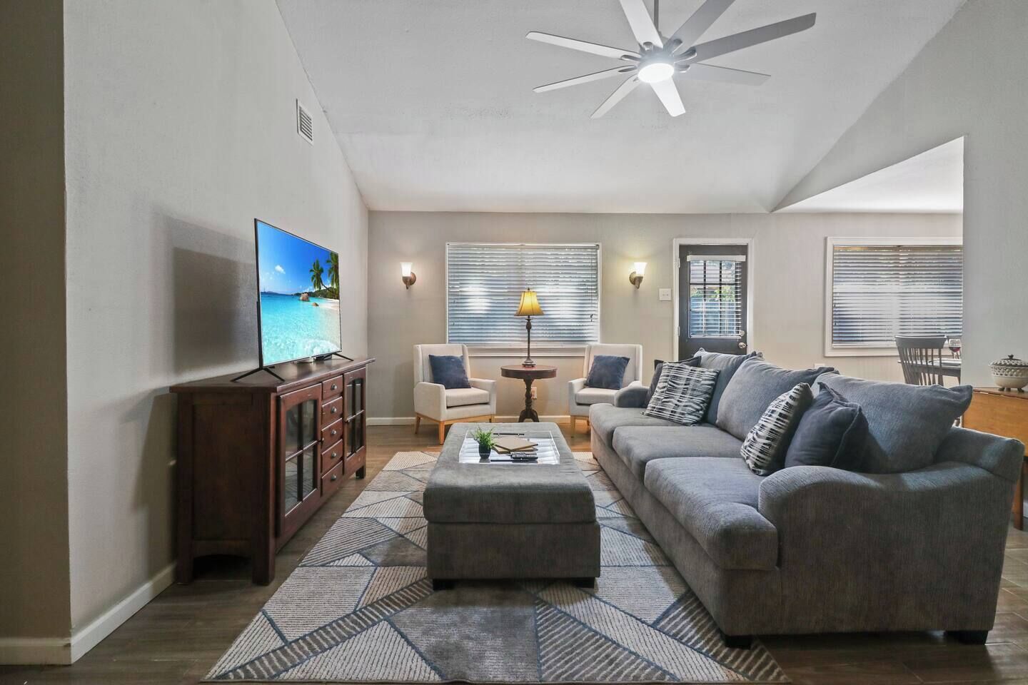 Un salon comprenant un téléviseur, un canapé, des fauteuils, une table basse et un ventilateur de plafond.