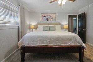 Une chambre à coucher avec un grand lit, deux lampes de chevet, un ventilateur de plafond et un tableau accroché au mur.