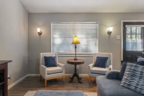 A living room with two armchairs, a round table with a lamp, and a sofa with a patterned pillow. - Woodlands 1 Story Retreat • 3BR • Game Room • Gym • Fenced Yard • Dining for 6 (Spring)