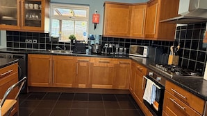A modern kitchen with wooden cabinets, a black tiled floor, and a built-in microwave. - Cosy 5-bed house in Swanley (Swanley)