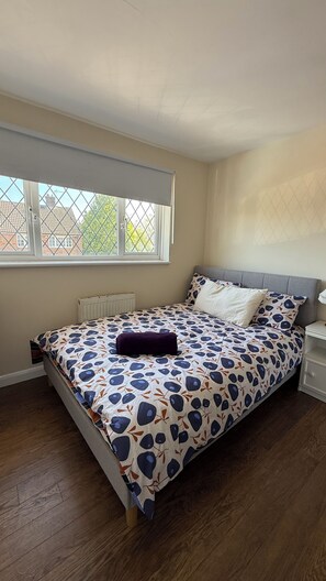 A bedroom with a bed, a window, a radiator, and a bedside table. - Cosy 5-bed house in Swanley (Swanley)