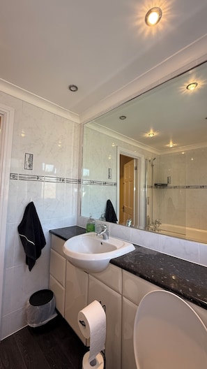 Uma casa de banho moderna com lavatório branco, um espelho grande e zona de duche.