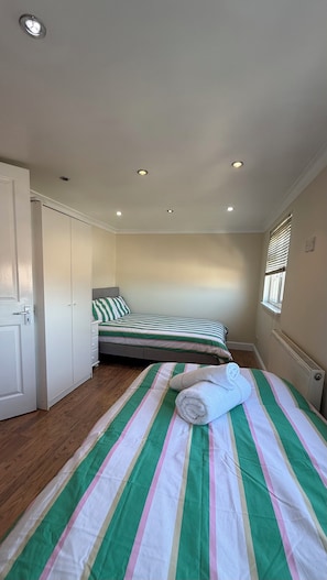 Quarto com duas camas de solteiro, guarda-roupa, radiador e janela com persianas.