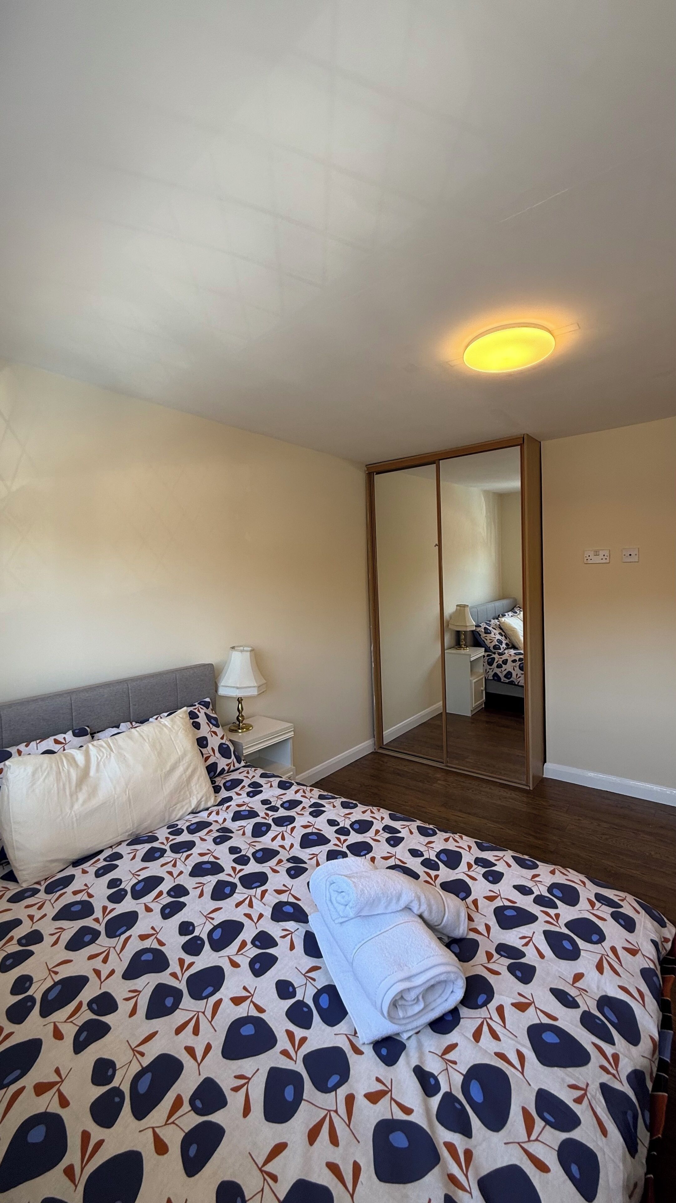 Quarto de hotel com cama, mesa de cabeceira, abajur e espelho.