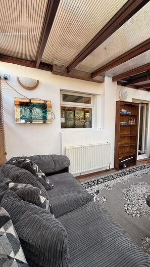 A room with a sectional sofa, a window, a radiator, and a wooden door. - Cosy 5-bed house in Swanley (Swanley)