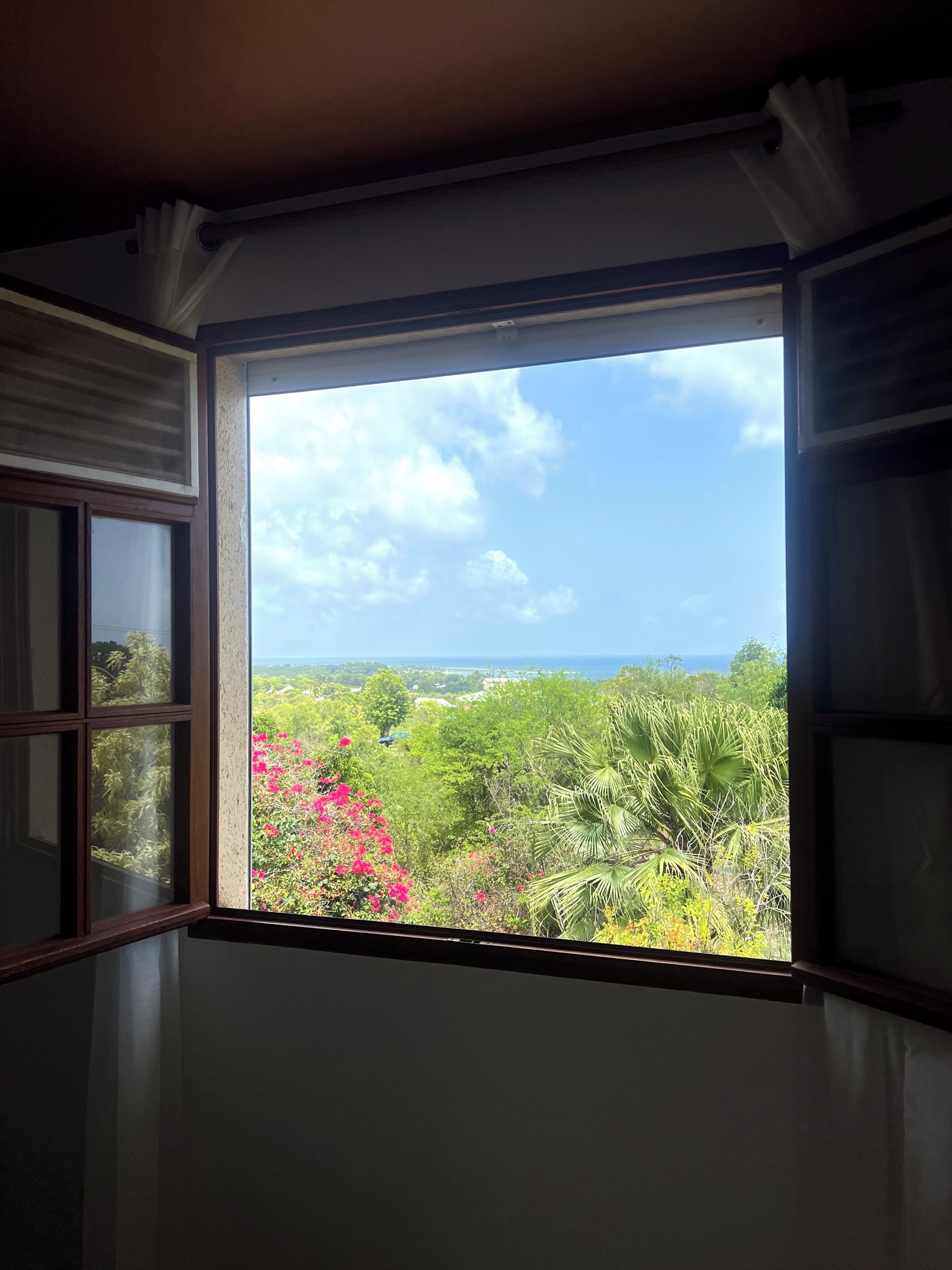 A room with a large window offering a view of a lush landscape with greenery and pink flowers.