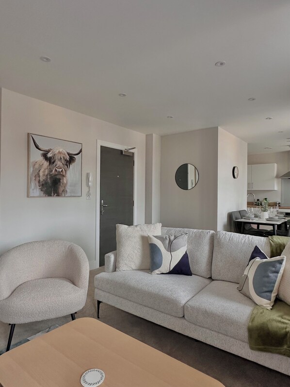 A modern living room with a sofa, armchair, and a dining table.