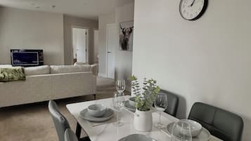 A dining area with a white table set for four, surrounded by black chairs. A clock is mounted on the wall above the table.