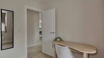 A room with a wooden desk, a white chair, a mirror, and a door leading to another room.