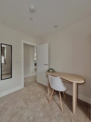 A room with a wooden desk, a white chair, a mirror, and a door leading to another room.