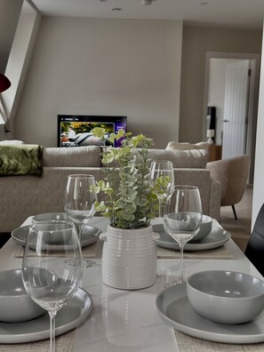 A dining area with a table set for four, a potted plant, and a television in the background.