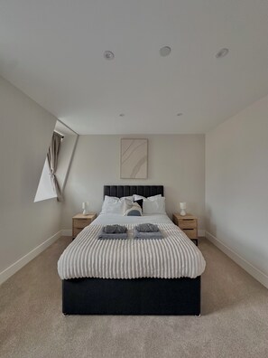 A modern bedroom with a black headboard, white bedding, and two bedside tables with lamps.