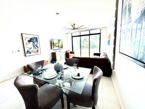 A dining area with a glass table, chairs, and a view of the outdoors through large windows. - N/H Luxe 2BR/2.5 BA Villa Ocean Views Pool & Gym (Reading)