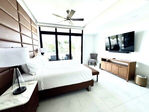 A modern hotel room with a bed, a TV, a ceiling fan, and a view of the outdoors. - N/H Luxe 2BR/2.5 BA Villa Ocean Views Pool & Gym (Reading)
