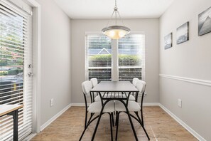 Uma sala de jantar com mesa, cadeiras, luminária pendente e janela com persianas.