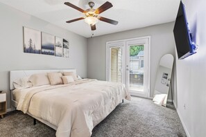 Quarto com cama, ventoinha no teto, televisão e porta com persianas.