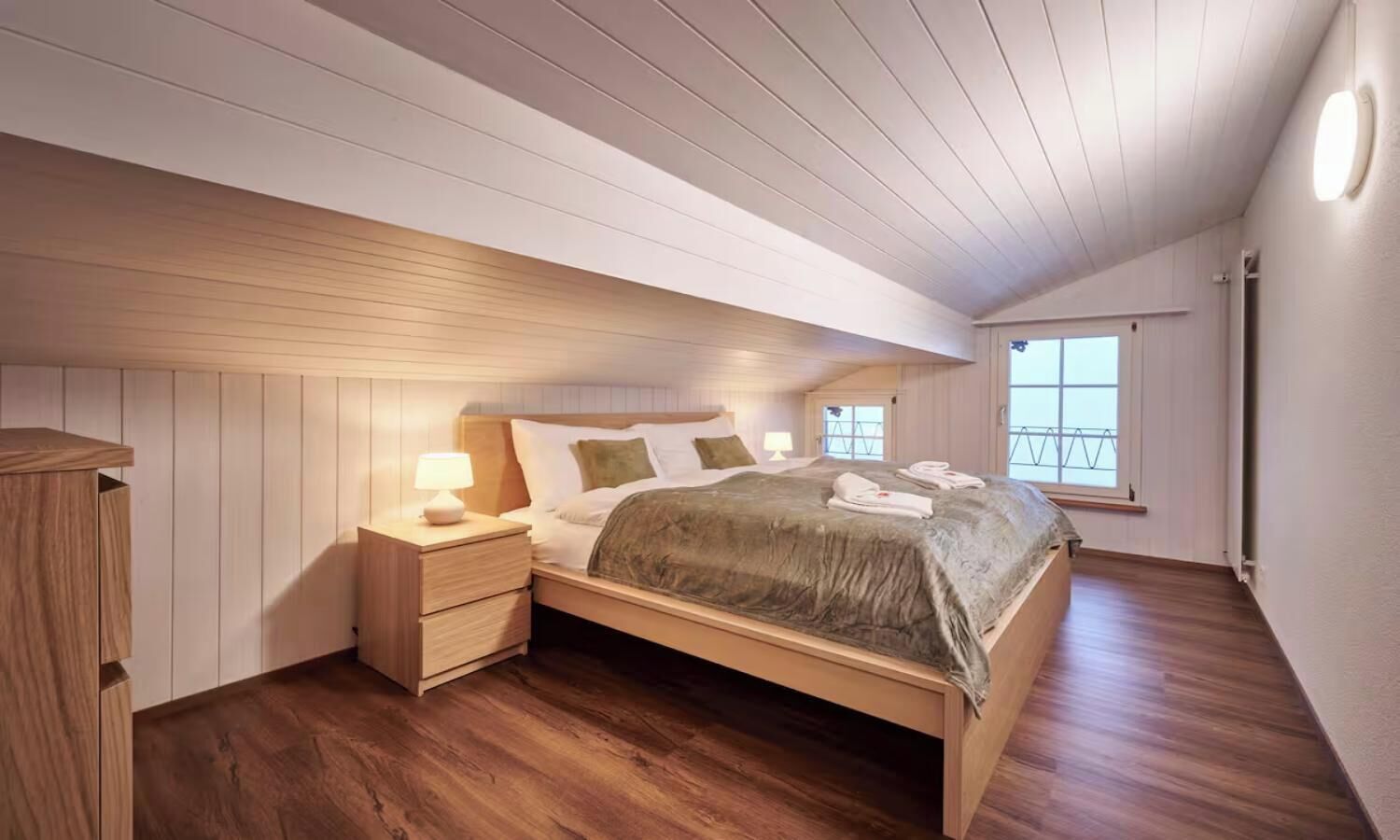 A bedroom with a wooden bed, bedside tables, and a window with a view.