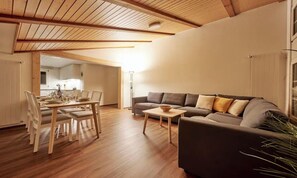 Un salon moderne avec un plafond en bois, un ensemble de canapés, une table à manger avec des chaises et un lampadaire.
