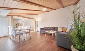 Ein modernes Wohnzimmer mit Essbereich, Holzboden und einem grauen Sofa.
