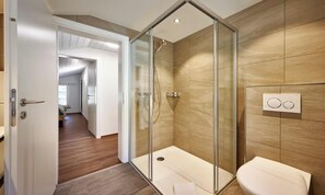 Ein modernes Badezimmer mit Duschkabine aus Glas, Toilette und einer wandmontierten Bedienkonsole.