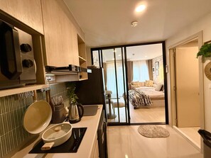 A compact kitchen with modern appliances, a dining area, and a view into a bedroom with a bed and curtains. - 1BR Pool & WiFi⁠ @ 10 min Patong Beach & Central (Tambon Kathu)