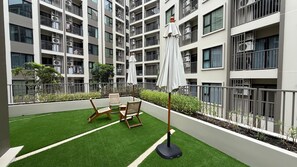 A multi-story residential building with balconies, air conditioning units, and outdoor seating with umbrellas. - 1BR Pool & WiFi⁠ @ 10 min Patong Beach & Central (Tambon Kathu)