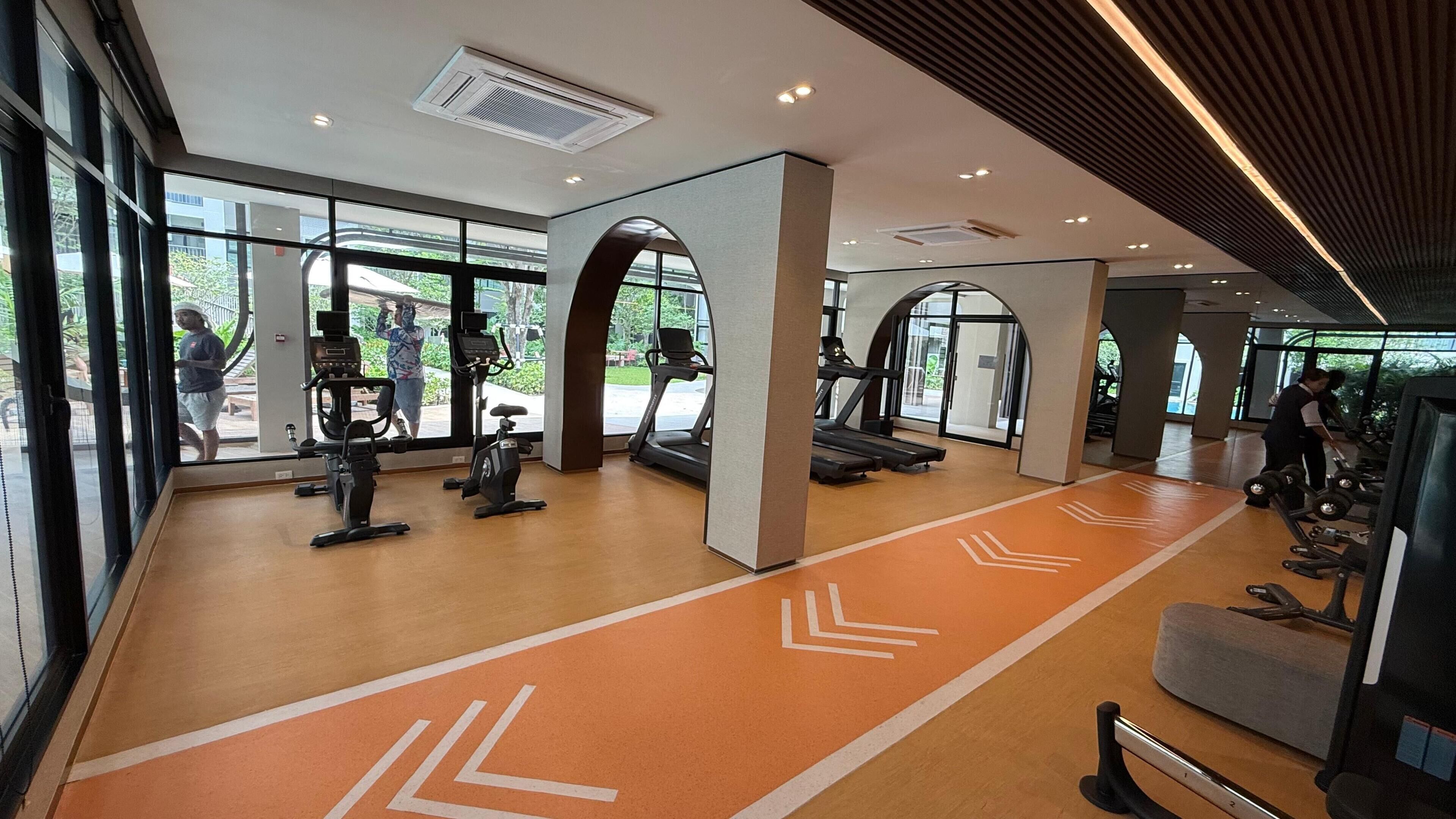 Une salle de sport équipée de matériel d’exercice, dotée de grandes fenêtres et d’un plancher en bois.