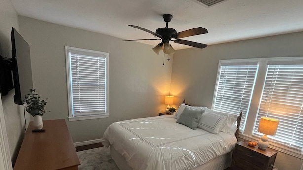 Un dormitorio con cama, ventilador de techo, mesita de noche con lámpara y cómoda.