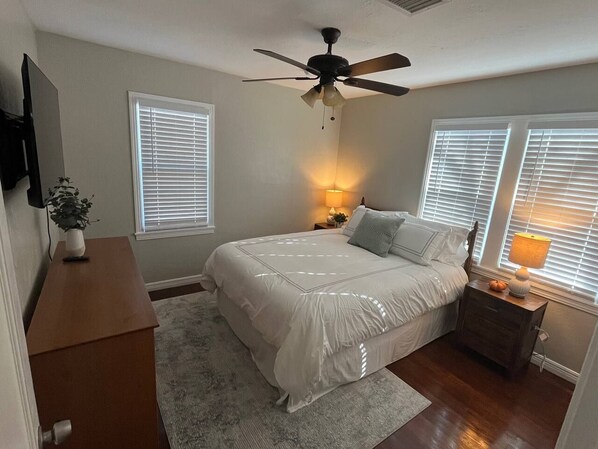 A bedroom with a bed, a ceiling fan, a nightstand with a lamp, and a dresser.